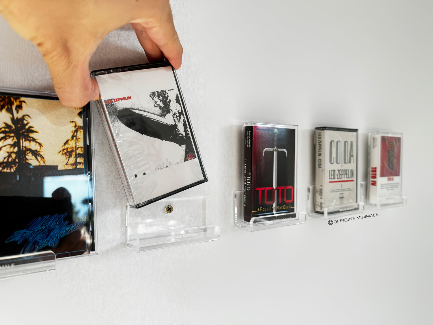 Collection of vintage cassette tapes on a white surface with a hand holding one tape.