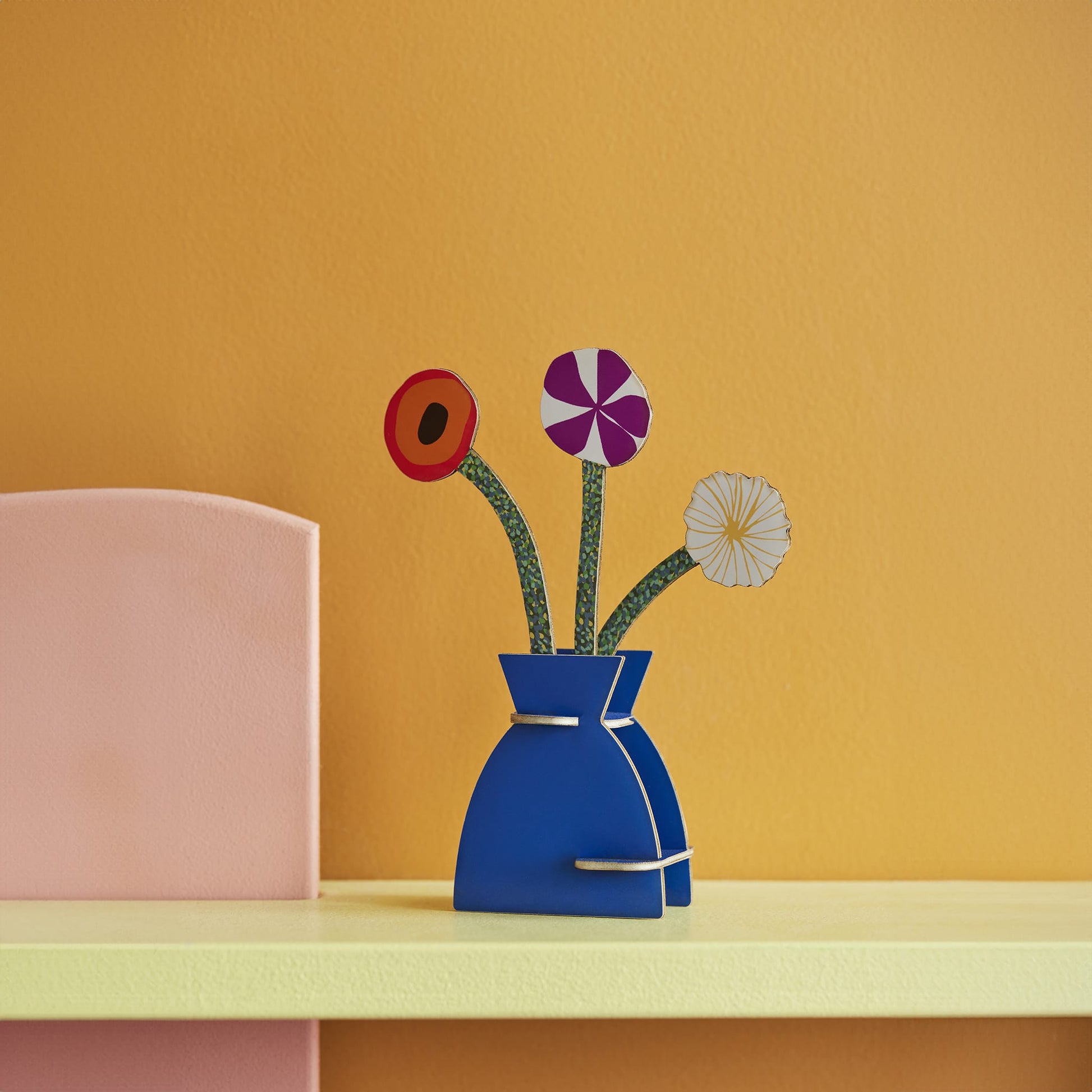 Blue vase with colorful flowers on a yellow surface against an orange wall