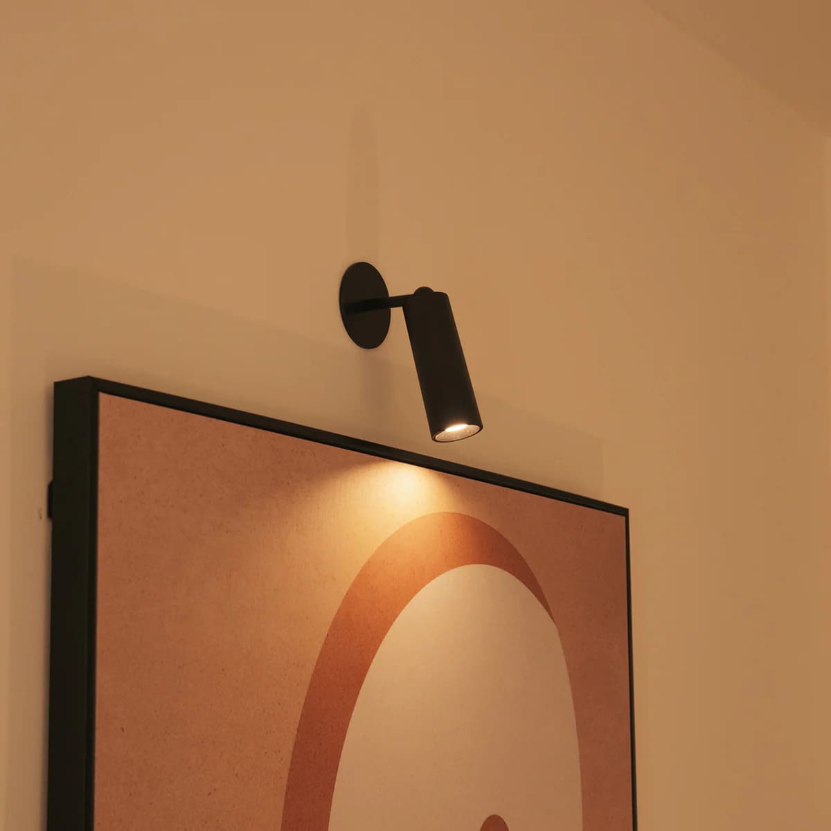 Modern wall light fixture on a wall with a framed abstract art piece below.