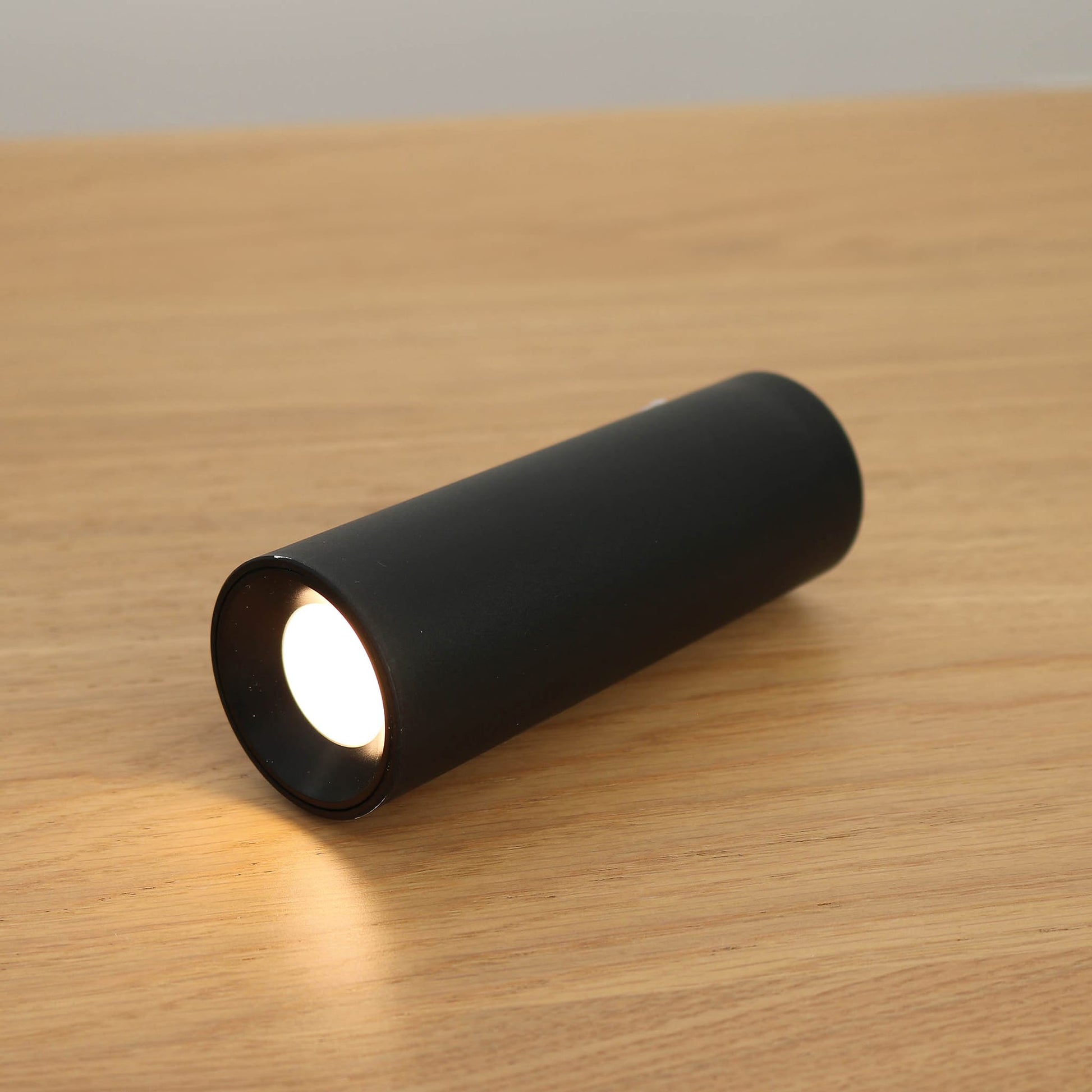 Black cylindrical light fixture on a wooden surface