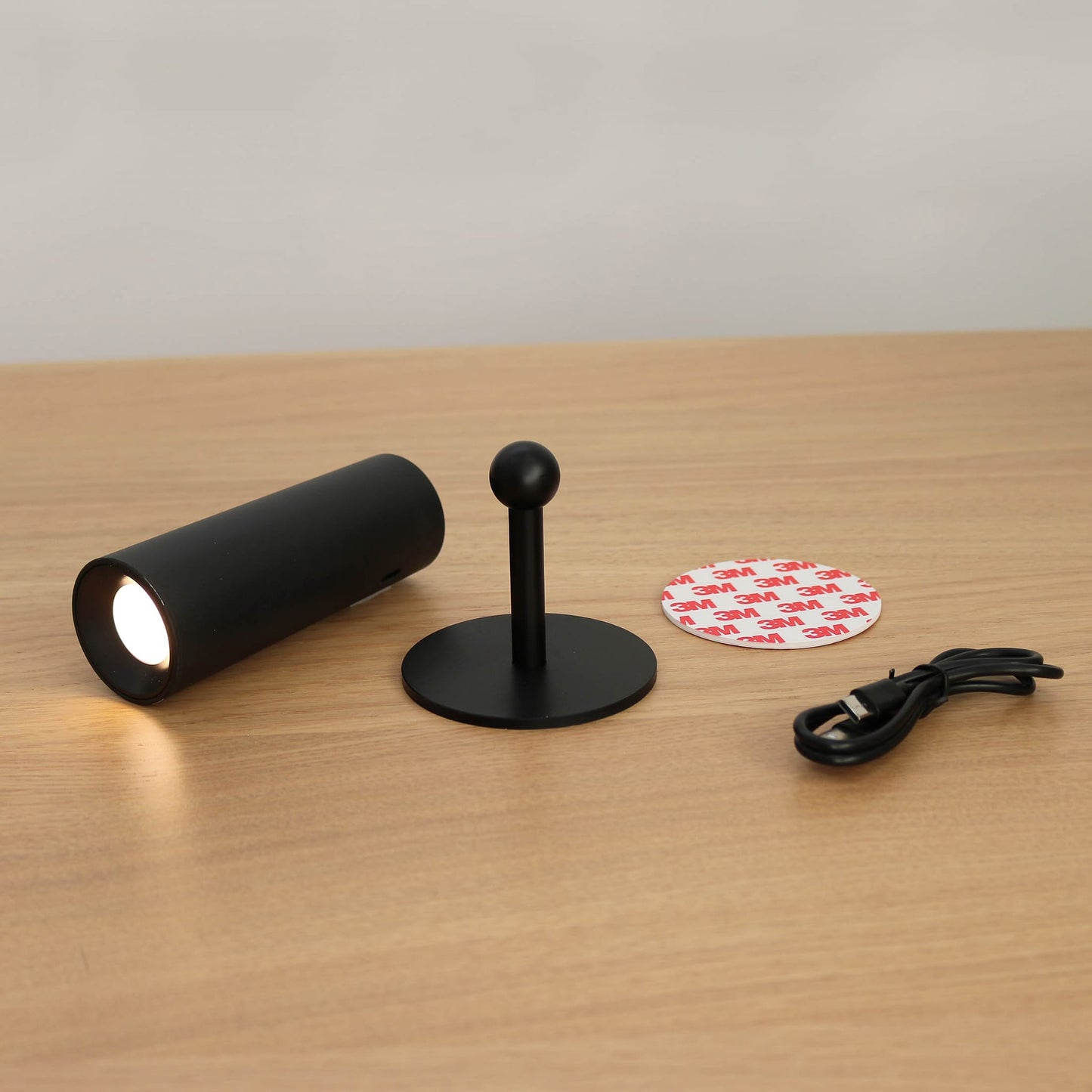 Black cylindrical light fixture with stand, cable, and circular component on a wooden surface.