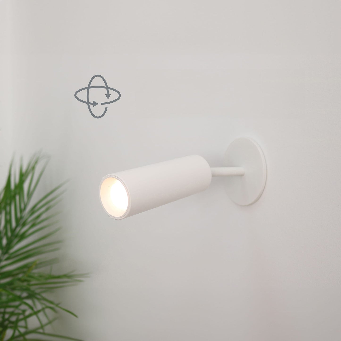 White wall-mounted light fixture on a light gray wall with a plant in the corner.